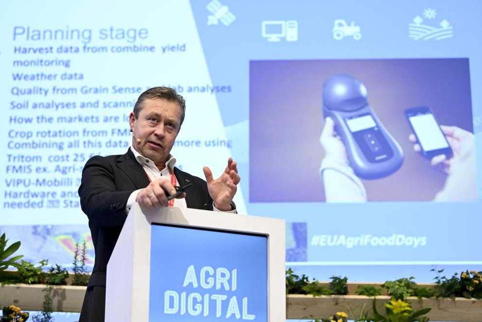 Max Schulman standing at a podium and a digital presentation in the background