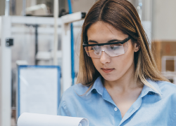 A young lady in protective goggles reads from a clipboard