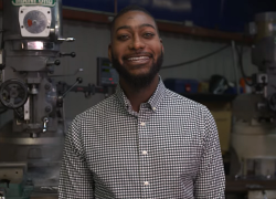 Ron Vargas, smiling, with manufacturing machinery and tools behind him