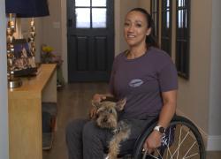 Vanessa Ross at home. She uses a wheelchair and is holding a small dog.