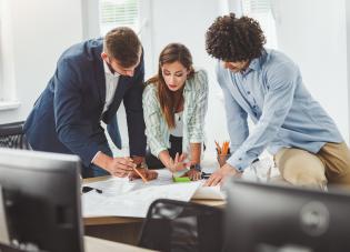 Tres empleados sentados en una mesa examinan un expediente. 