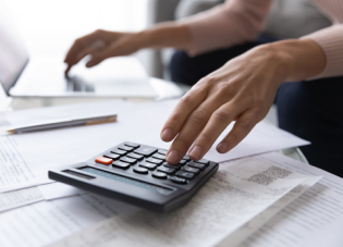 Close up photo of a woman's hands as she reviews retirement planning papers with her computer and calculator nearby