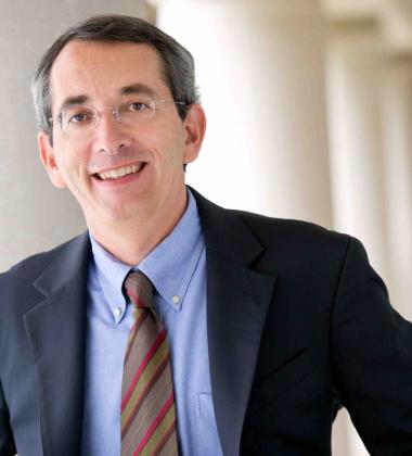 Richard Saver headshot in a long hallway with columns behind him