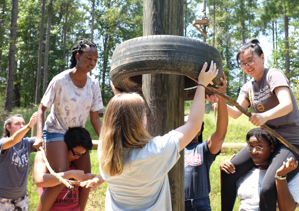 A group of female and male students helping each other on an obstacle course.