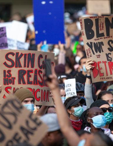 Un grand groupe de personnes tenant des pancartes avec des slogans en anglais qui disent, entre autres, « Les vies noires comptent », « Assez, c’est assez » et « Votre silence est une trahison ». Visibilité masquée.