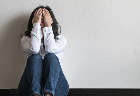 Female sitting on the floor with her back to a wall covering her face