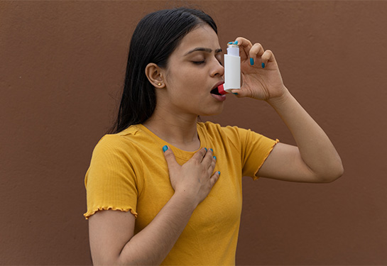 Woman taking deep breath and holding an inhaler to her mouth.