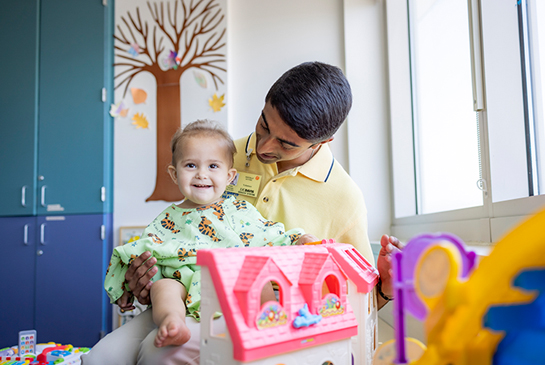 A student volunteer holding a small child in a playroom.