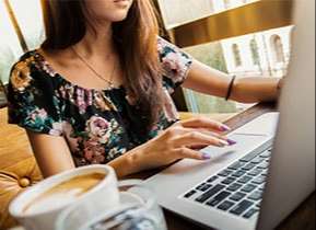 Girl typing on laptop computer with coffee next to her