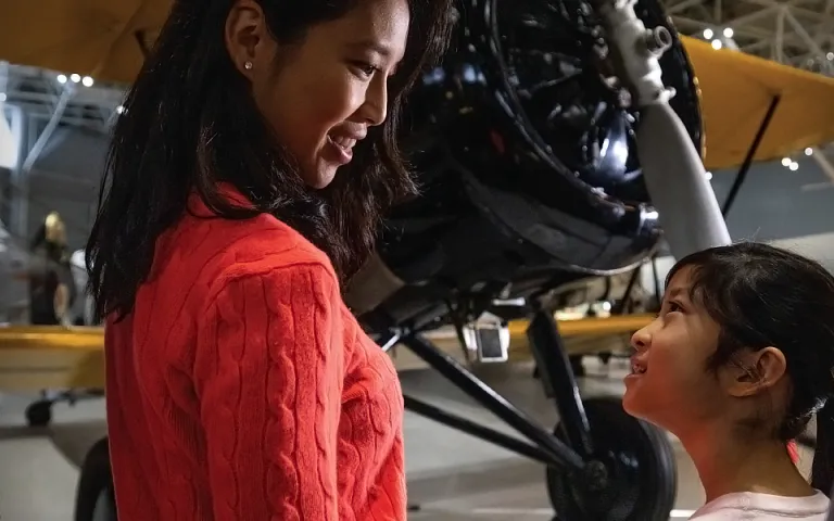 Une fille et une femme se parlent et sourient. Elles se tiennent devant un avion jaune au Musée de l'aviation et de l'espace du Canada.