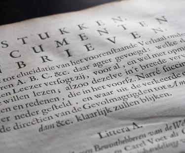 Detail of a printed book shows a page with text in Dutch.