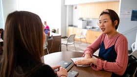 Two graduates sit at a table in conversation