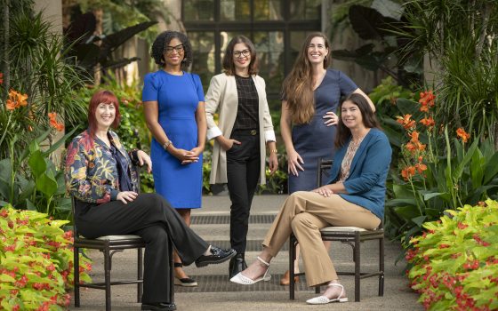 A group of 5 people, some sitting, some standing, in a garden setting.