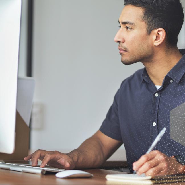 Male employee in front of a computer, taking notes and engaging with content on screen.