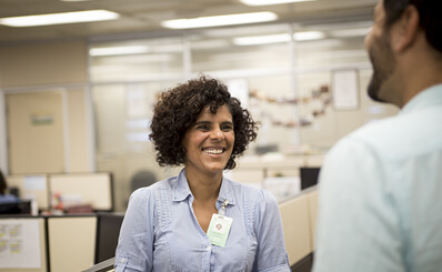 Mulher sorrindo e conversando com colega no escritório