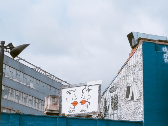 Gebäude vor denen ein Plakat mit zwei Gesichtern und der Aufschrift STAY HUMAN zu sehen sind