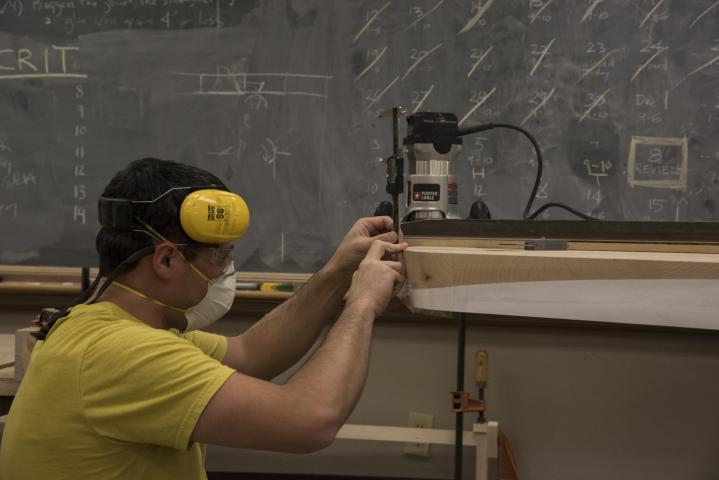 A student stoops down to look at their woodworking project.