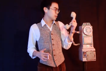 man with glasses and a vest holds a rotary phone in one hand and a cigarette in the other