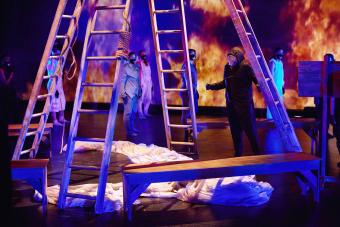 dancer wearing a mask clenches his fists, standing under ladders