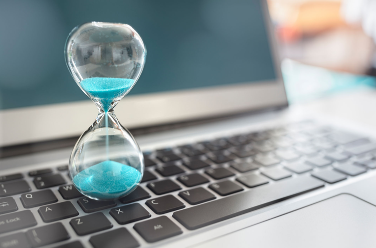 Hourglass timer over halfway done with blue sand sitting on an Apple computer keyboard