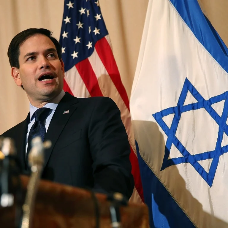 U.S. Sen. Marco Rubio (R-FL) speaks into a microphone, in front of U.S. and Israeli flags