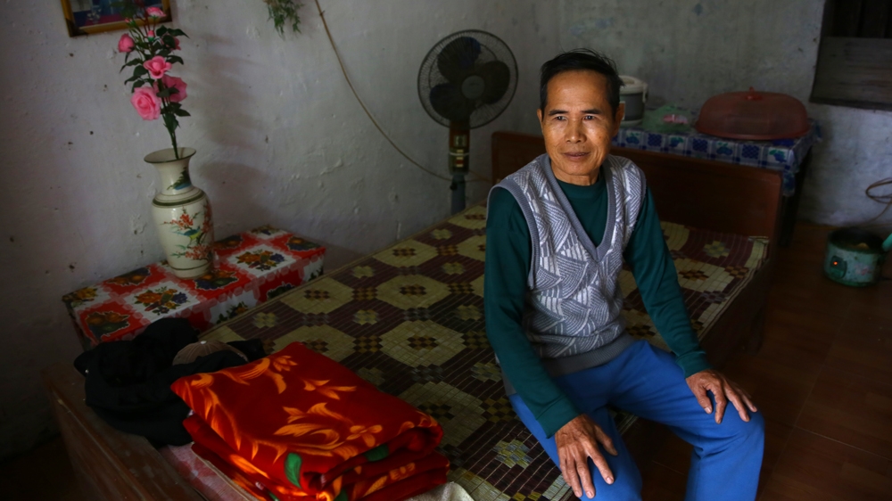 Veteran Lai Chan Chinh, 68, sits on a bed in his room in the warehouse of a local cooperative in Thanh Liem district, Ha Nam province. Chinh served in the North Vietnamese army from 1960 to 1975. His relatives say he now suffers from paranoia related to his wartime experiences [Na Son Nguyen/Al Jazeera] 