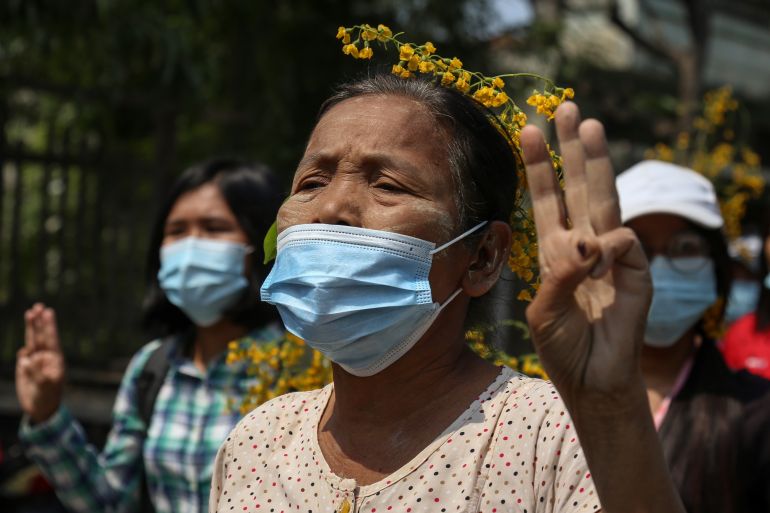 An older woman, her face covered with a blue mask, holds thgree fingers aloft to show support for Myanmar's anti-coup movement