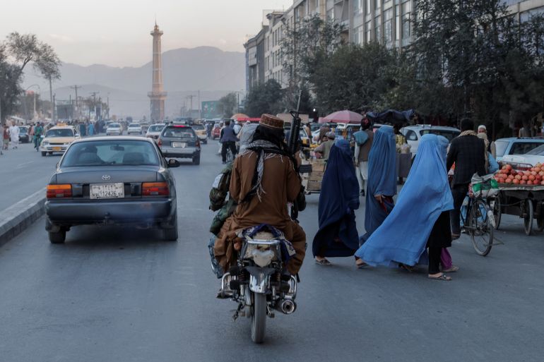 A group of women wearing burqas crosses the street as members of the Taliban drive past in Kabul, Afghanistan