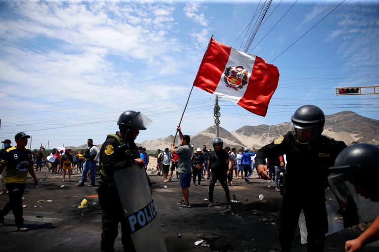 Supporters of Castillo wave a Peruvian flag during a protest. There are armed police in the foreground.