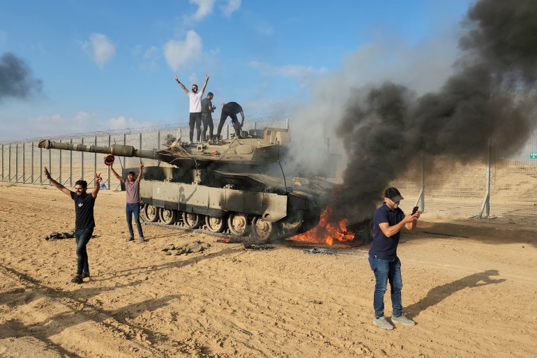 Palestinians celebrate by a destroyed Israeli tank at the Gaza Strip fence east of Khan Younis