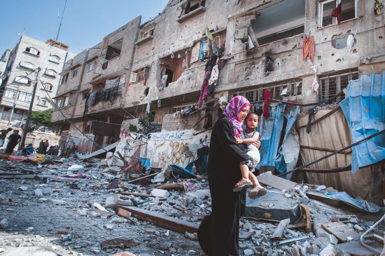 A Palestinian mother holds her son while passing a severely damaged residential building that was destroyed overnight by an Israeli airstrike at Al Sheikh Redwan in Gaza City on July 10, 2014 [Courtesy of Eman Mohammed]