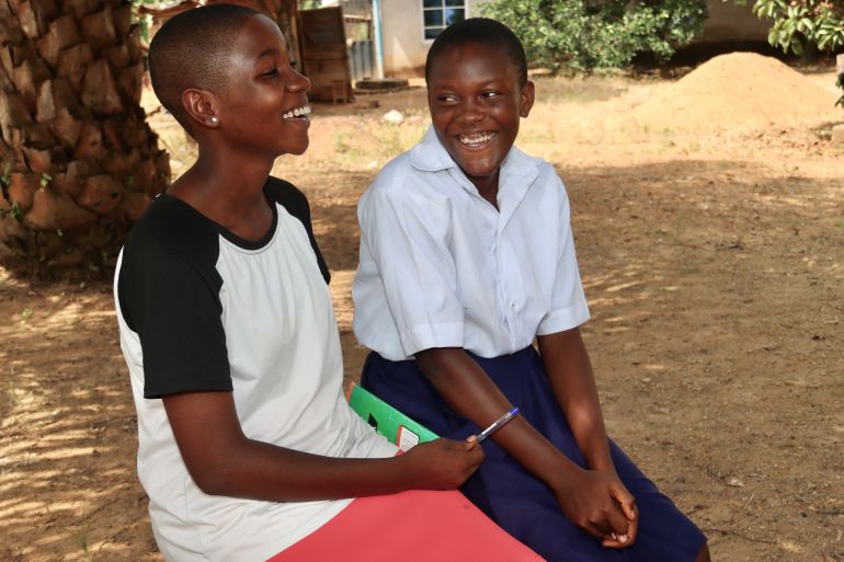 A photo of Rebecca (left) and Blessing sitting next to each other with a notebook between them and with Rebecca holding a pen in one hand.