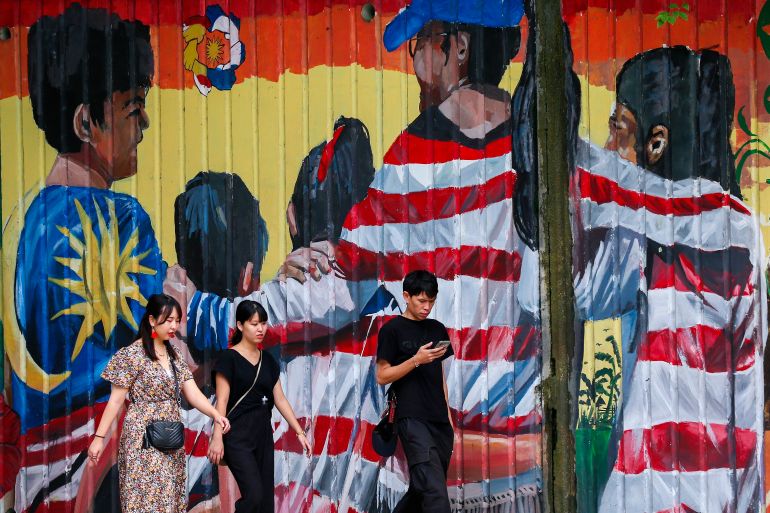 People walking in front of a wall painted with the Malaysian flag