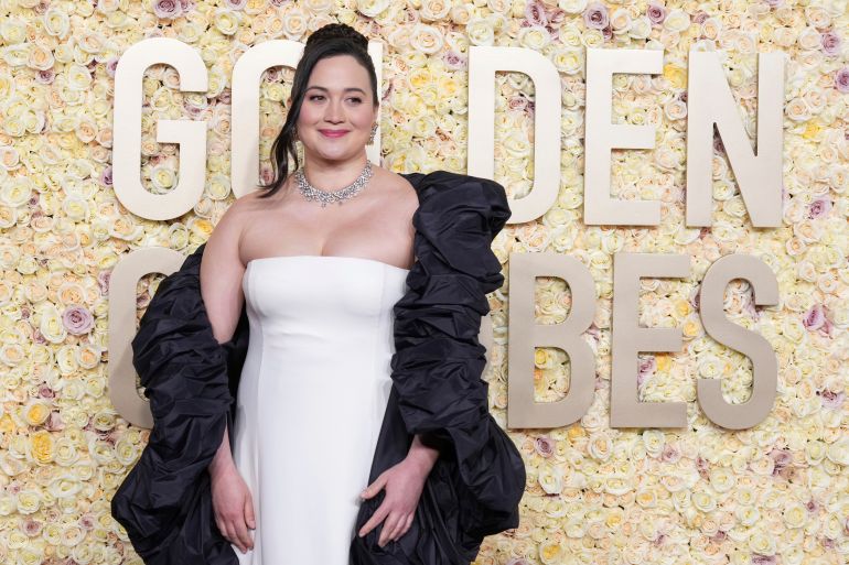 Lily Gladstone on the red carpet. She is wearing a white dress with a black shawl