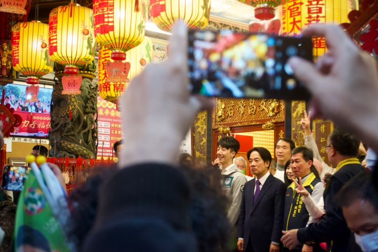 William Lai at a temple in Taiwan. There are lots of people around. He can be seen in the gap between the arms of someone holding up their phone to take a picture