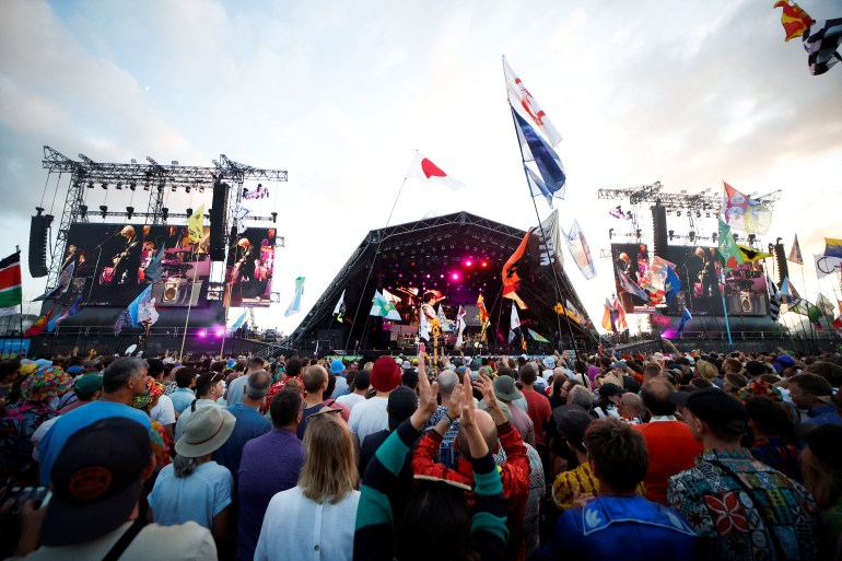 The crowd at Worthy Farm in Glastonbury. There are lots of people in front of the stage. There are flags and pennants