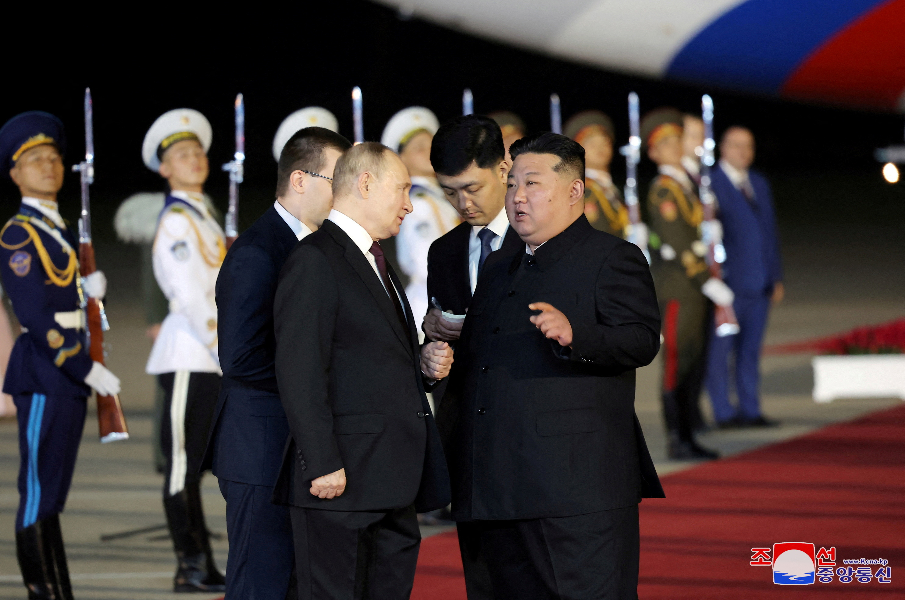 Kim Jong Un greeting Vladimir Putin at the airport. They're on a red carpet. There is an honour guard behind them. Kim is talking.