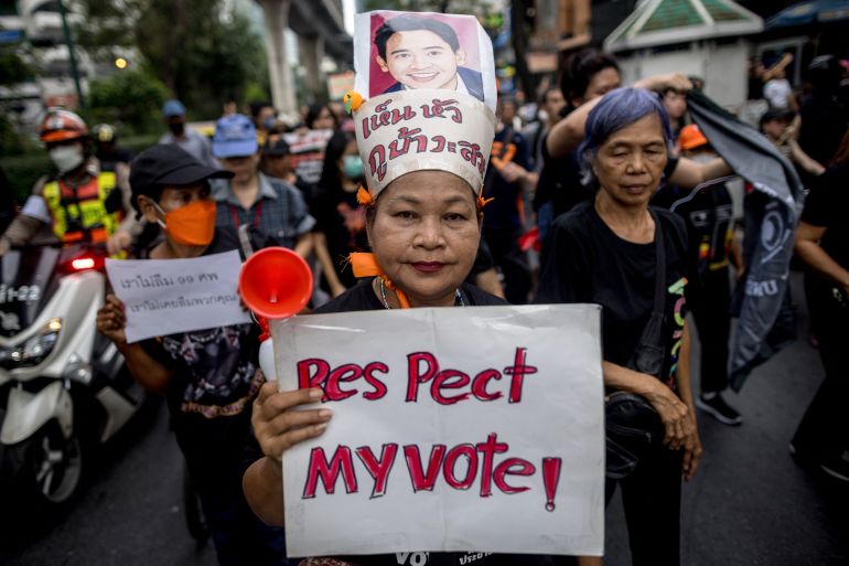 A pro-democracy protester holds a sign reading 'Respect my Vote'. Sh is wearing a headdress and lots of other people are around her.