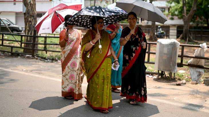 Women carrying umbrellas arrive to cast their ballots to vote at a polling station in Dhanbad, in India's Jharkhand