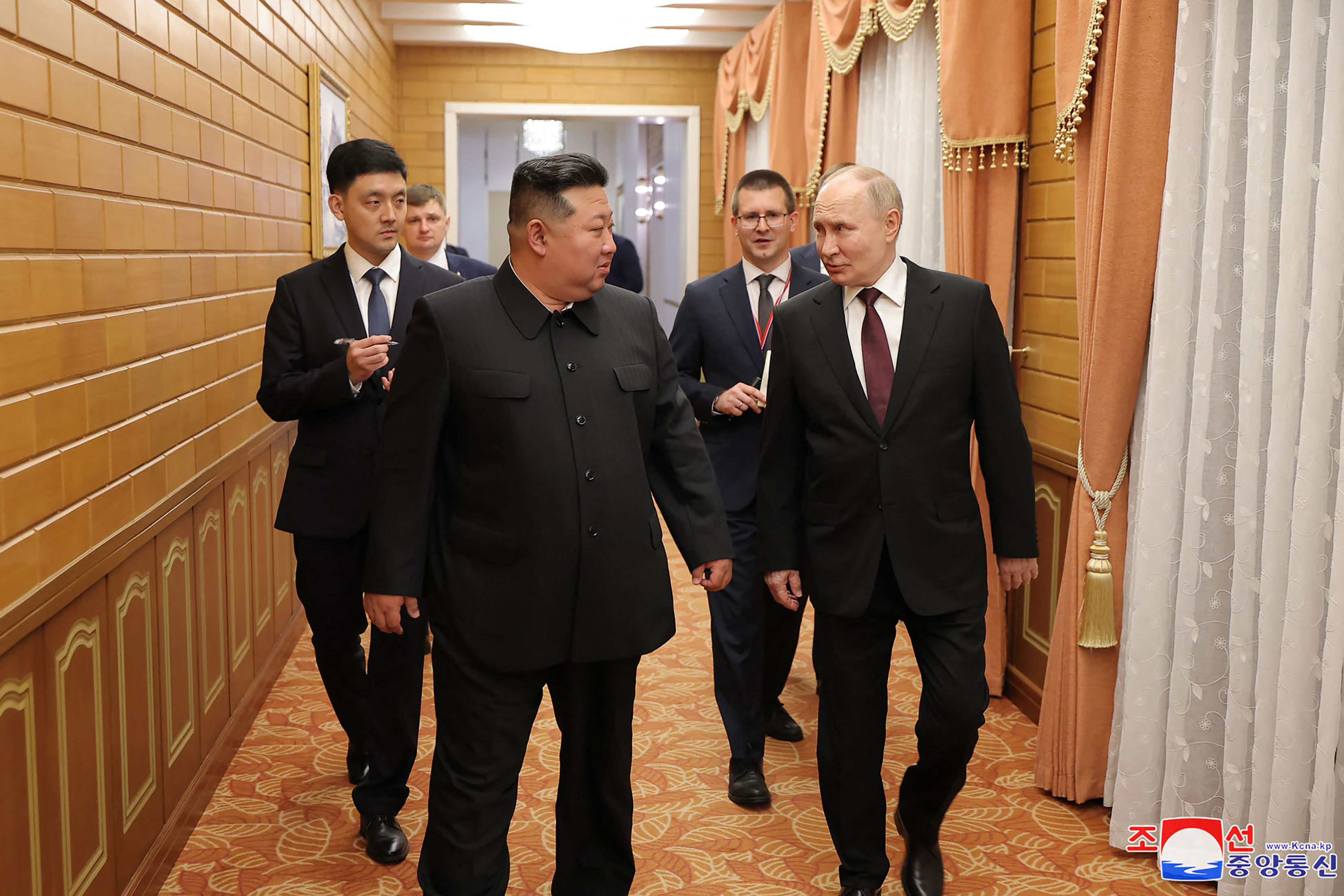 Putin and Kim smiling and chatting as they walk along a corridor in the Kumsusan State Guest House in Pyongyang. Officials are walking behind them.