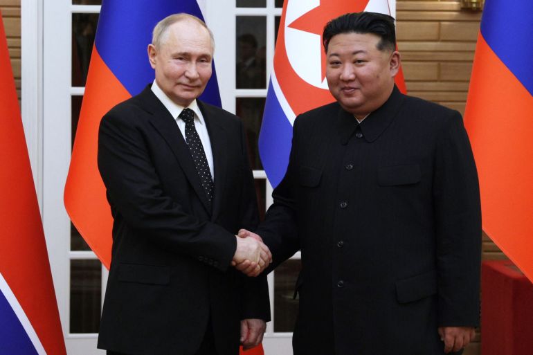Kim and Putin shaking hands in front of their countries' flags. They are smiling.