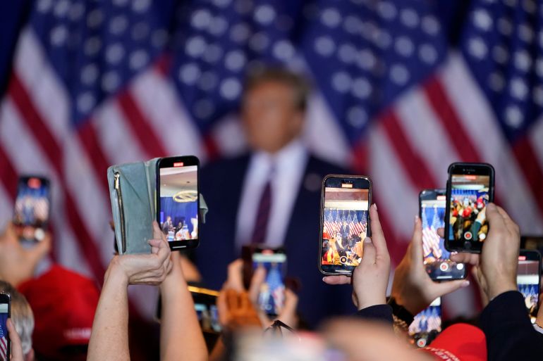 Supporters lift their cellphones to record Donald Trump on stage, surrounded by US flags.