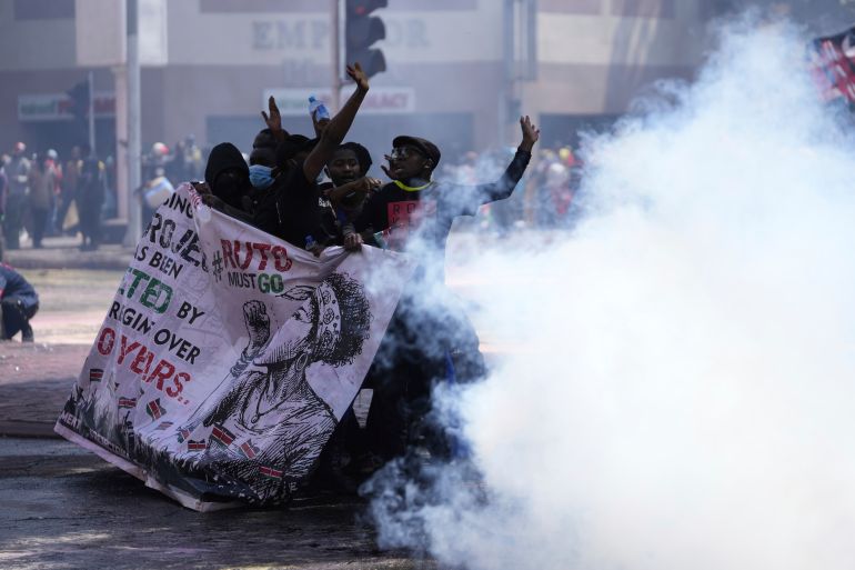 Protesters hide behind a banner as police fire tear gas at them during a protest over proposed tax hikes in a finance bill in downtown Nairobi
