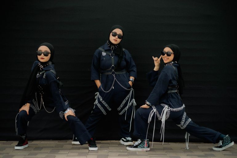 Marsya, Siti and Widi. They are dressed in black and wearing sunglasses. They have chains around their waists and spiked collars at their necks. They are also wearing black headscarves.