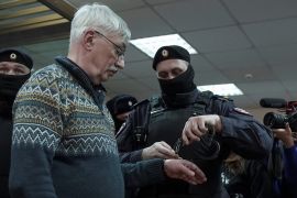 A Russian police officer puts handcuffs on Oleg Orlov during a court hearing in Moscow, in which he was sentenced to two and a half years in prison [File: Tatyana Makeyeva/Reuters]