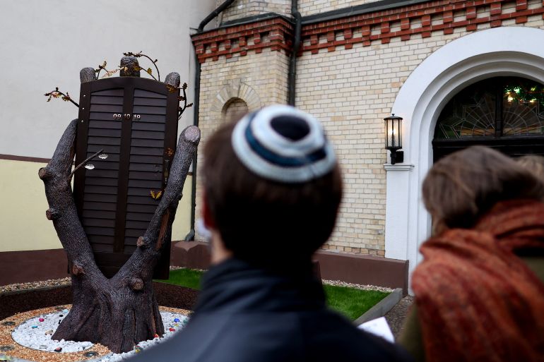 People stand next to a new memorial made of the original entrance door inside the synagogue in Halle, eastern Germany, on October 09, 2020, on the first anniversary of the anti-Semitic attack on the synagogue. Last year's attack on the synagogue in Halle came on October 9 during Yom Kippur, the holiest day in the Jewish calendar, and was one of the worst acts of anti-Semitic violence in Germany's post-war history. Two people were shot dead after an extremist tried and failed to storm a synagogue. The 28-year-old neo-Nazi suspect is currently on trial for the crime. (Photo by Ronny Hartmann / AFP)