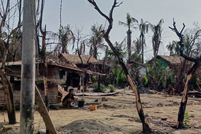 This photo taken on May 21, 2024 shows a woman cooking next to destroyed houses and burned trees following fighting between Myanmar's military and the Arakan Army (AA) ethnic minority armed group in a village in Minbya Township in Rakhine State. - The charity Doctors Without Borders will halt medical activities in northern Rakhine state in Myanmar due to an "extreme escalation of conflict" between an ethnic armed group and the military, it said on June 27. (Photo by AFP)