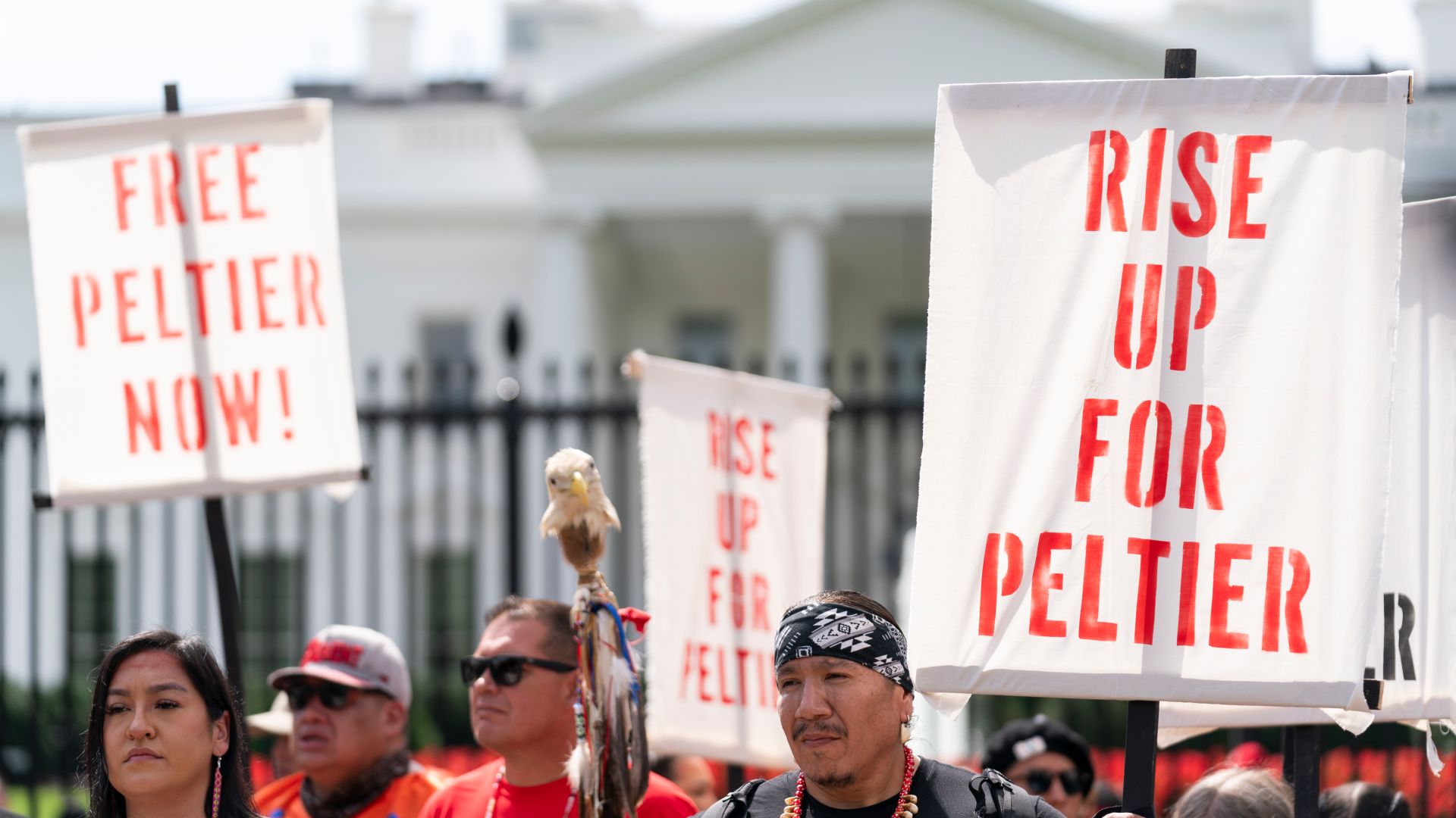 Protesters stand outside the wrought iron gate of the White House, holding up signs that read, "Rise up for Peltier."