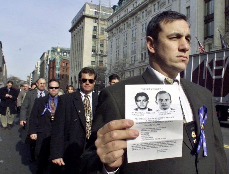 FBI agents protest outside the White House, marching in a line. One holds up a black-and-white photo of two agents killed at Pine Ridge Reservation in South Dakota.