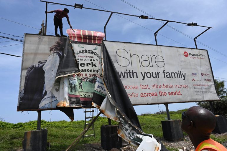 Workers dismantle an advertisement board to protect it from Hurricane Beryl in Kingston